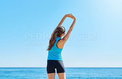 Buy stock photo Shot of a young woman stretching while out on the beach on a sunny day