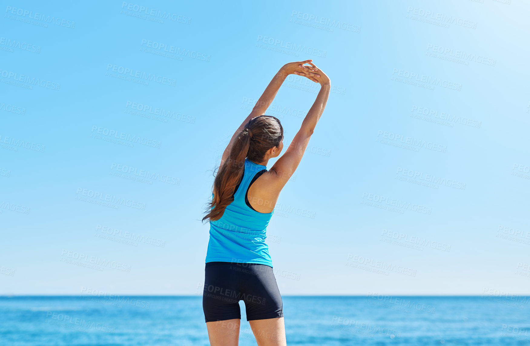 Buy stock photo Shot of a young woman stretching while out on the beach on a sunny day