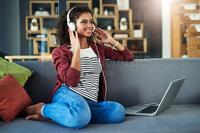 Buy stock photo Shot of a young woman using headphones and a laptop on the sofa at home