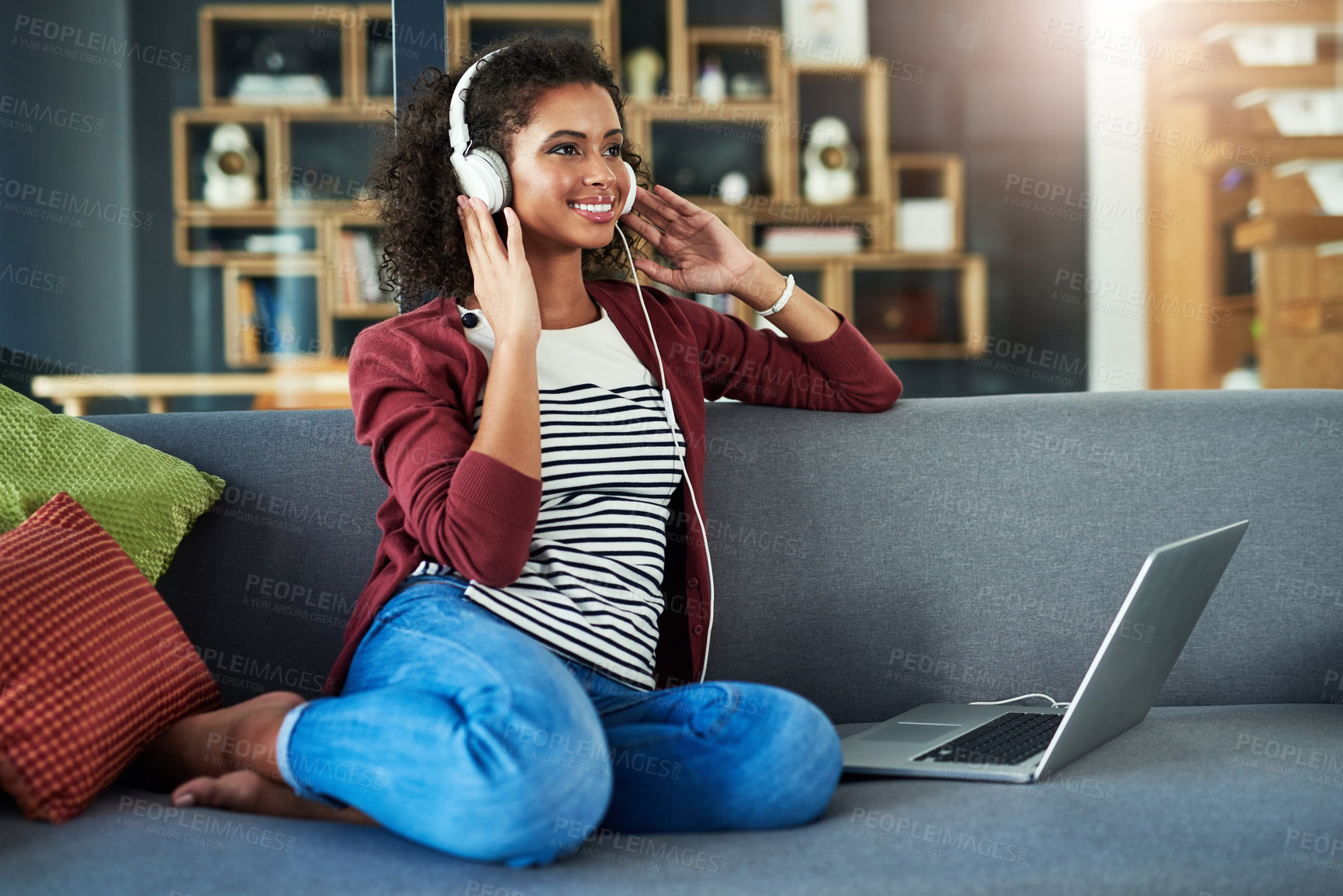 Buy stock photo Shot of a young woman using headphones and a laptop on the sofa at home