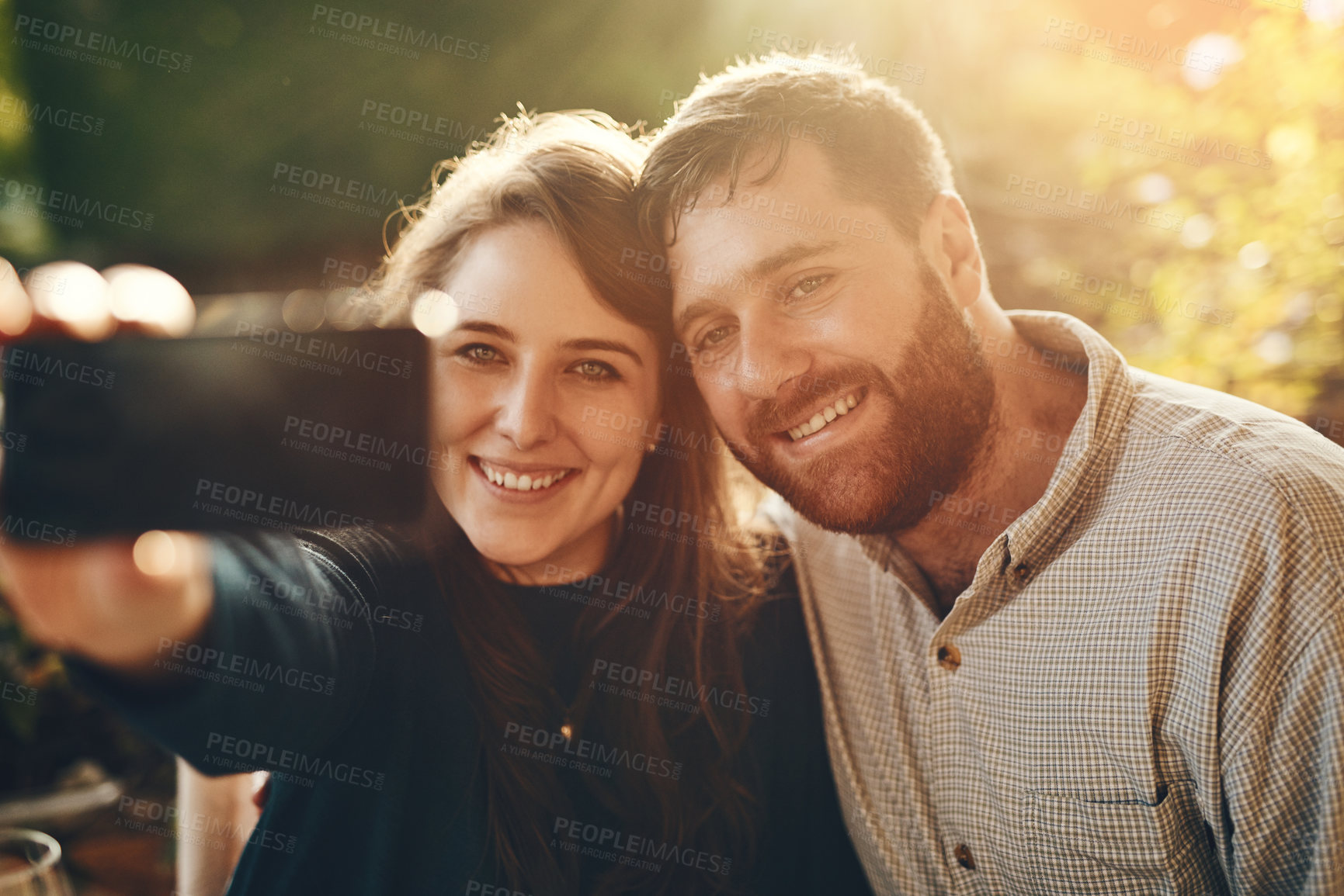 Buy stock photo Happy, phone and couple love to take a selfie at an outdoor restaurant for a romantic date in spring. Relax, memory and young woman taking pictures with a young partner smiles on marriage anniversary