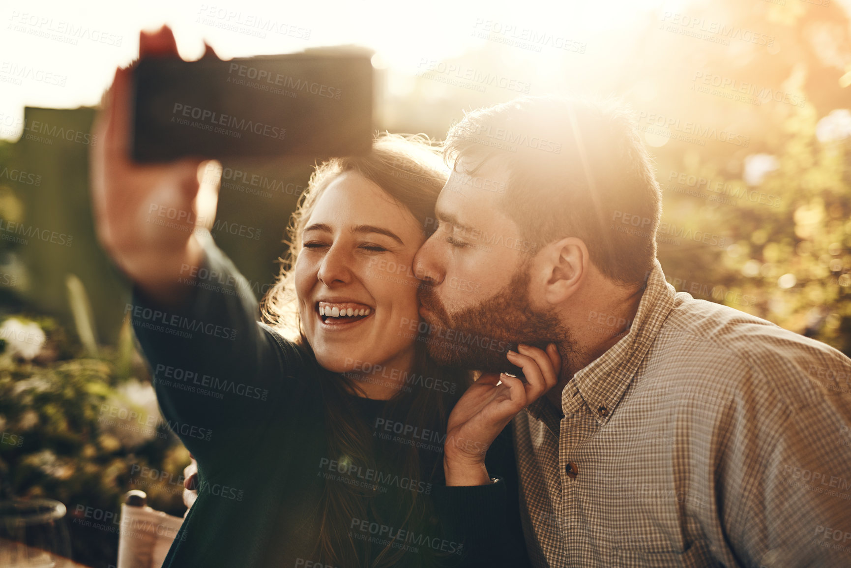 Buy stock photo Couple, kiss and phone for happy selfie, love or relationship bonding moments together in nature. Man and woman with smile for loving romance, travel or vacation photo with smartphone in the outdoors