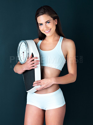 Buy stock photo Studio portrait of an attractive young woman holding a scale against a dark background