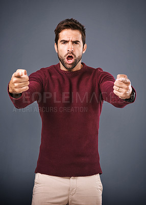 Buy stock photo Studio shot of a handsome young man pointing his fingers in anger against a gray background