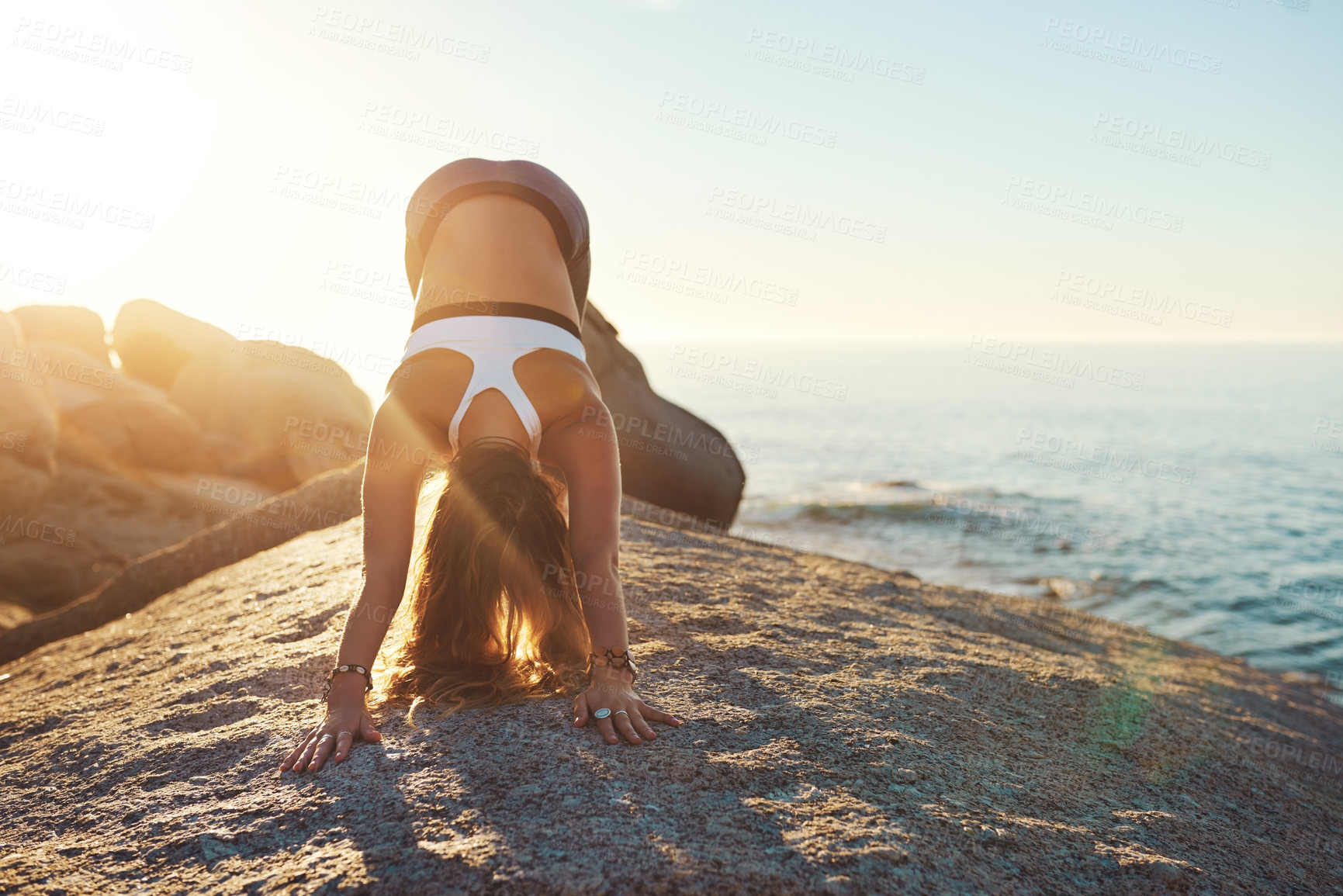 Buy stock photo Yoga, downward pose and woman by ocean for wellness, health and fitness in nature. Morning, pilates and person on rock by sea for exercise, training and stretching for calm, balance and flexibility