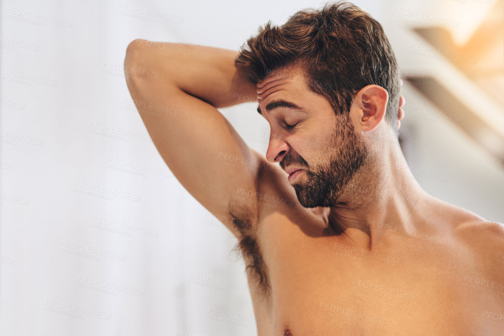 Buy stock photo Cropped shot of a handsome young man smelling his armpits while standing in his bathroom at home