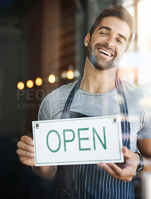 Buy stock photo Shot of a handsome young man hanging up an open sign on the door of his store
