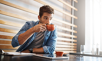 Buy stock photo Shot of a handsome young man drinking coffee while working in a coffee shop