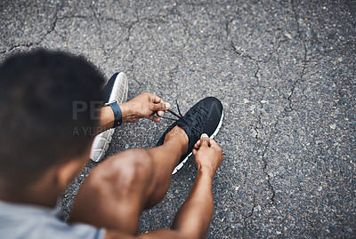 Buy stock photo High angle shot of a sporty man tying his shoelaces while exercising outdoors