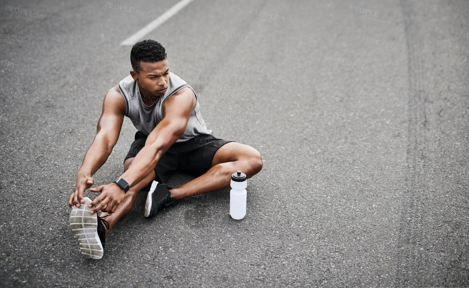 Buy stock photo Shot of a sporty young man stretching his legs while exercising outdoors