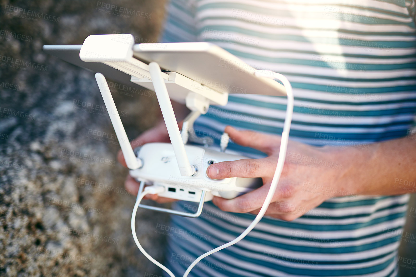 Buy stock photo Closeup of an unrecognizable man holding a remote control and using it to fly a drone outside on a beach during the day