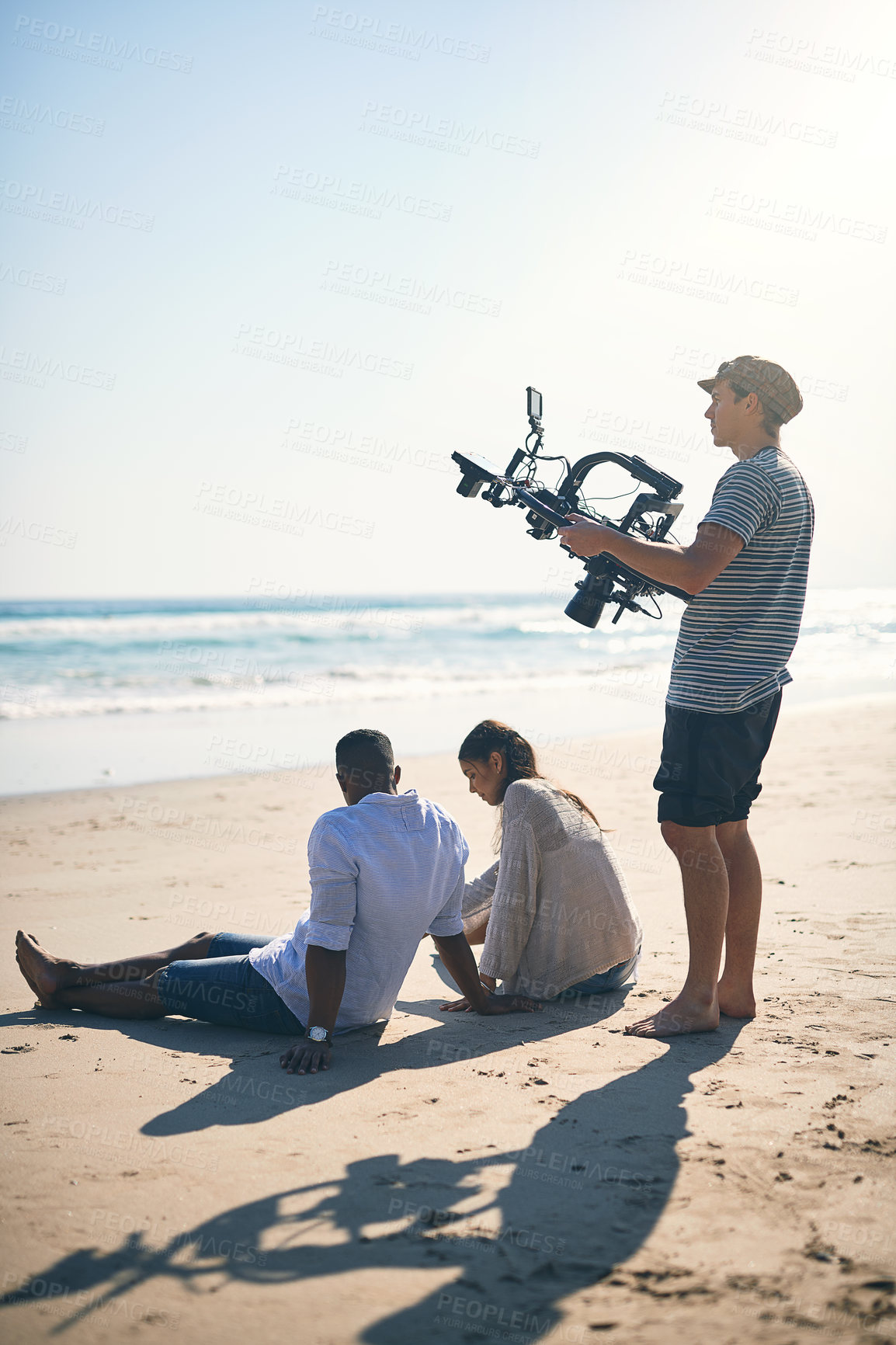 Buy stock photo Shot of a focussed young man shooting a closeup scene with a state of the art video camera outside on a beach during the day