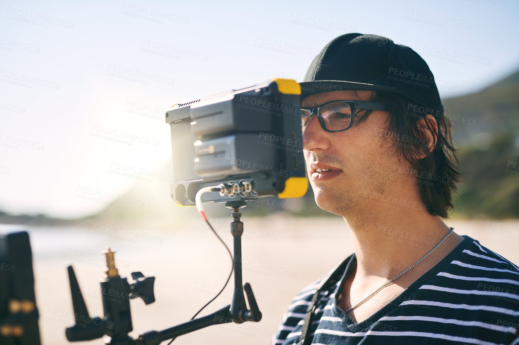 Buy stock photo Shot of a focused young man shooting a scene with a state of the art video camera outside on a beach during the day