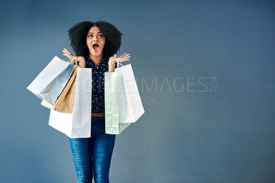 Buy stock photo Studio portrait of a young woman carrying shopping bags and looking surprised against a blue background