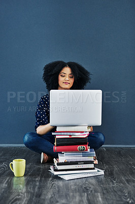 Buy stock photo Studio shot of a young woman using a laptop with books stacked in front of her against a blue background