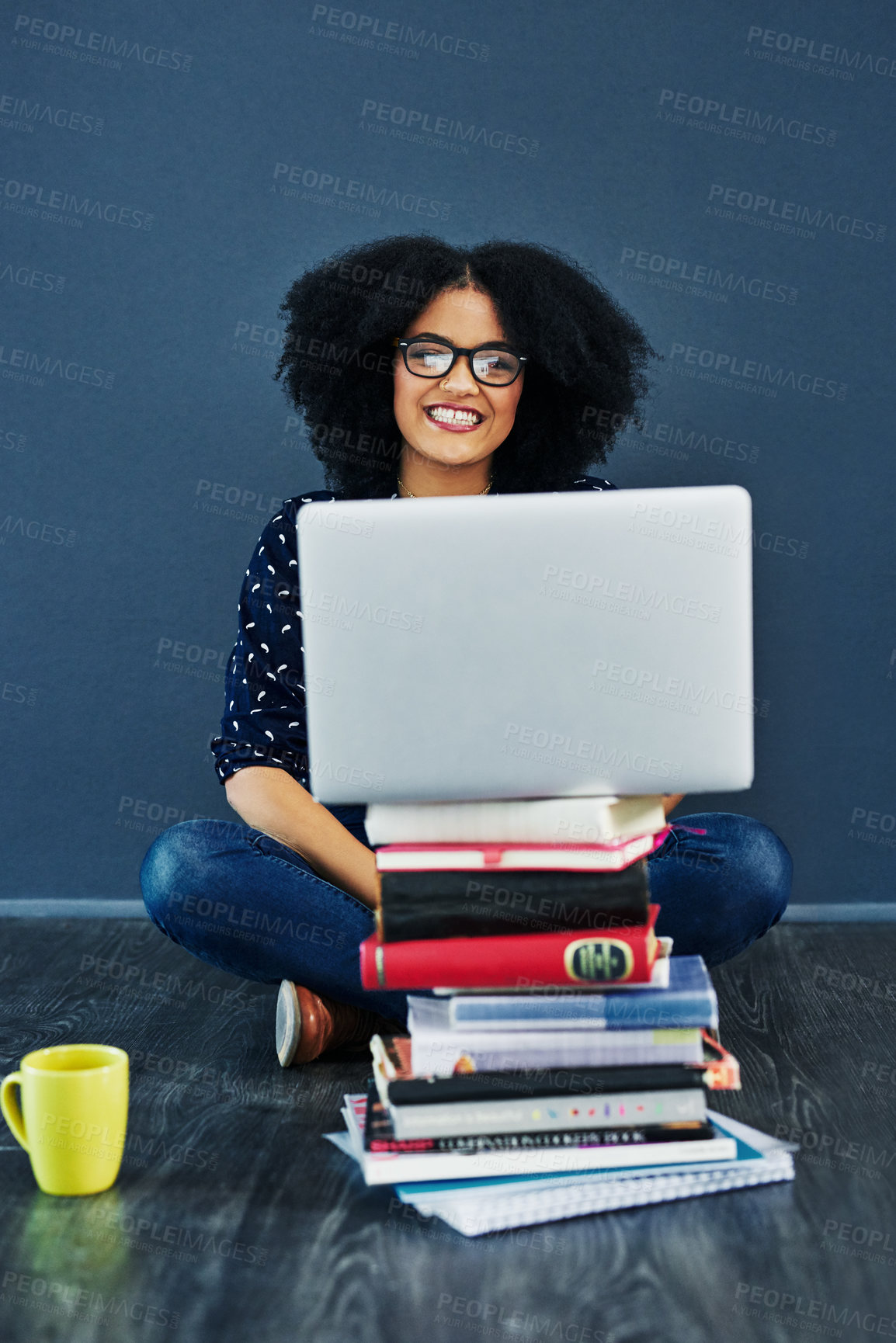 Buy stock photo Studio shot of a young woman using a laptop with books stacked in front of her against a blue background