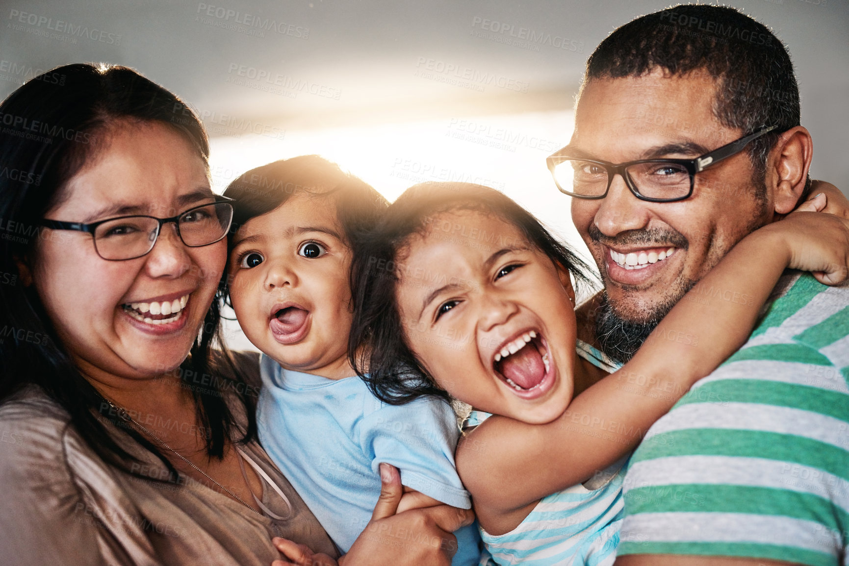 Buy stock photo Portrait of a cheerful young family standing together while looking into the camera  inside at home during the day