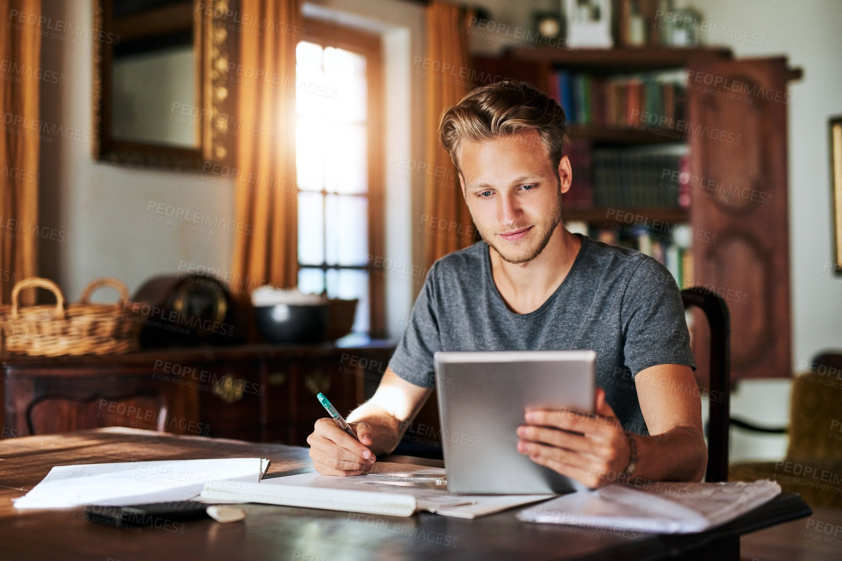 Buy stock photo Shot of a young man using a digital tablet while working on a project at home