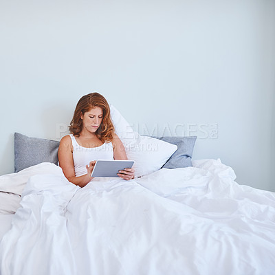 Buy stock photo Shot of a young woman using a digital tablet while relaxing in bed at home