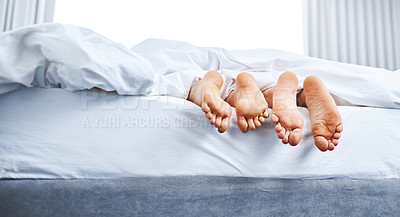 Buy stock photo Rear view shot of a couple's bare feet sticking out underneath the bedsheets at home