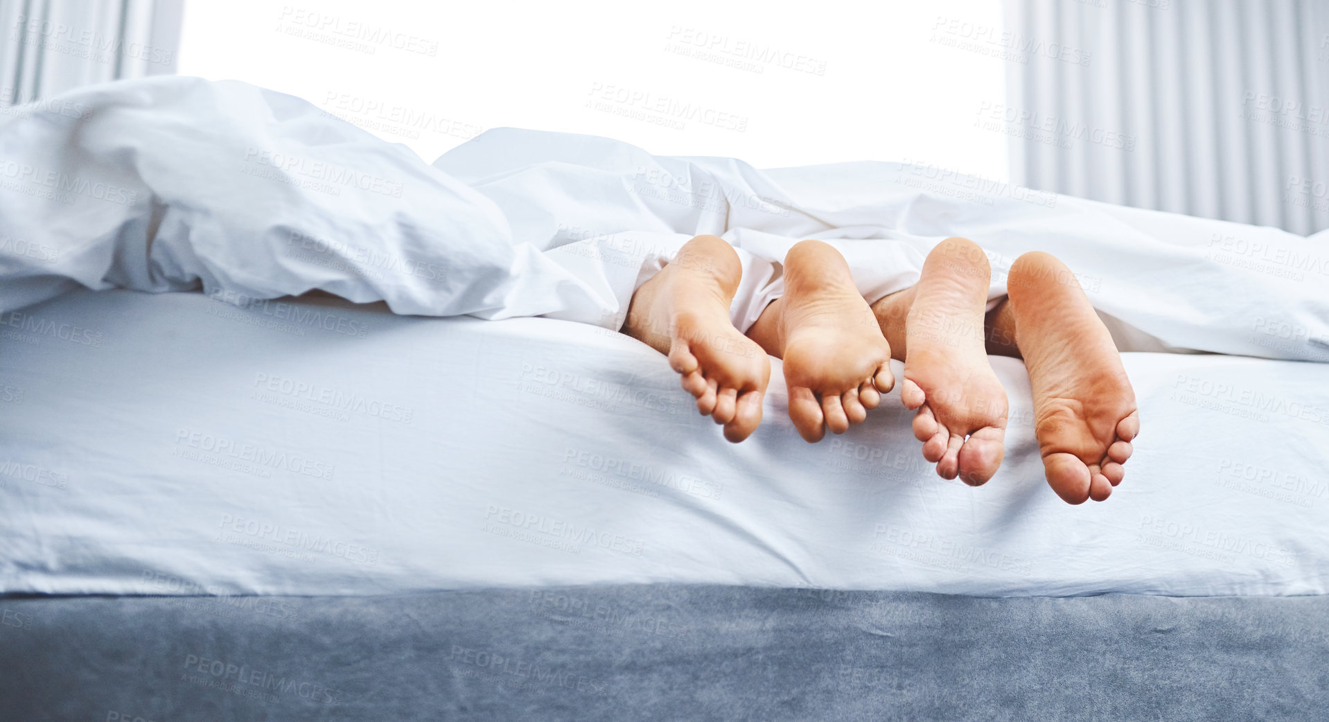 Buy stock photo Rear view shot of a couple's bare feet sticking out underneath the bedsheets at home