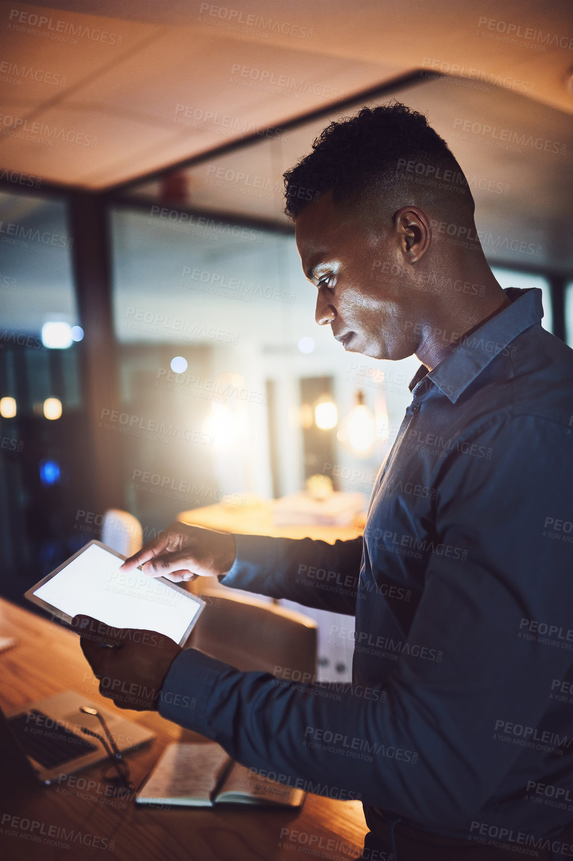 Buy stock photo Cropped shot of a handsome young businessman using his tablet while working late at night in a modern office