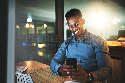 Buy stock photo Cropped shot of a handsome young businessman sending a text message while working late at night in a modern office