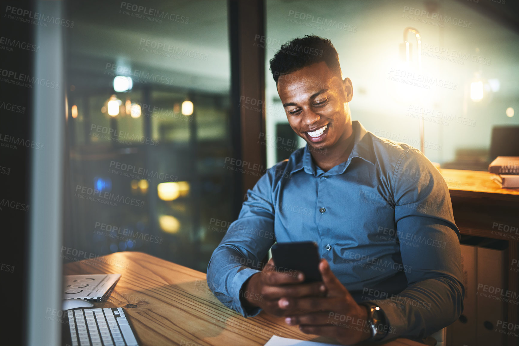 Buy stock photo Cropped shot of a handsome young businessman sending a text message while working late at night in a modern office