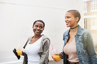 Buy stock photo Shot of two young women walking in the city laughing while holding their cool drinks