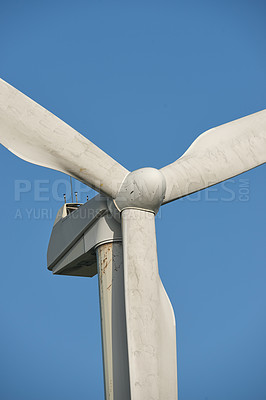 Buy stock photo Windmill turbine for generating electricity against a blue sky background outside. Converting kinetic energy into a sustainable, renewable and clean source of power with propellor blades