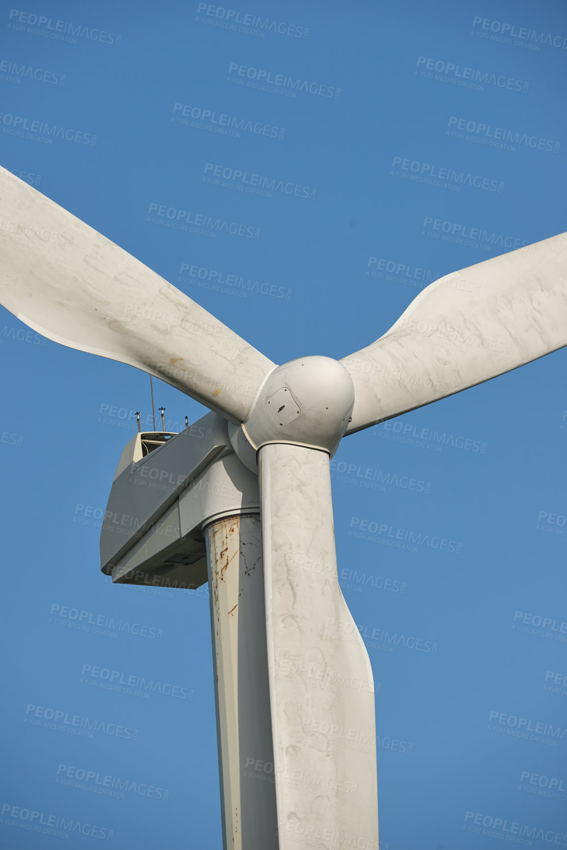 Buy stock photo Windmill turbine for generating electricity against a blue sky background outside. Converting kinetic energy into a sustainable, renewable and clean source of power with propellor blades