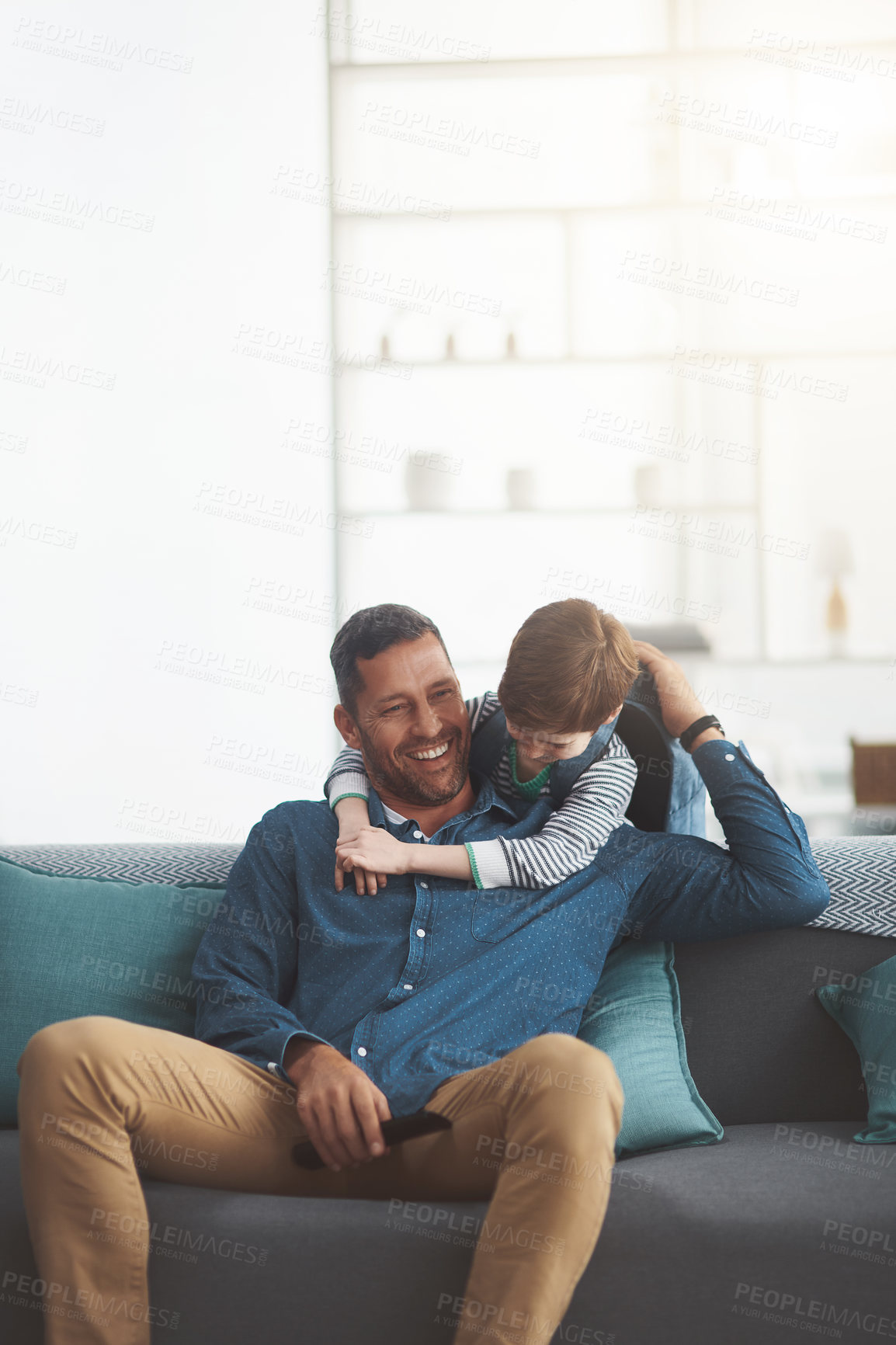 Buy stock photo Shot of a cheerful little boy and his father playing around together while being seated on a sofa together at home