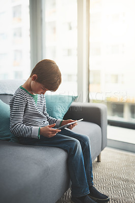 Buy stock photo Shot of a focused little boy browsing on a digital tablet while being seated on a sofa at home during the day