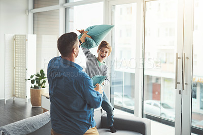 Buy stock photo Shot of a cheerful little boy and his father having a pillow fight together in the living room at home during the day