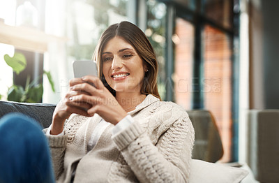 Buy stock photo Shot of an attractive young woman sending text messages while relaxing on her sofa at home