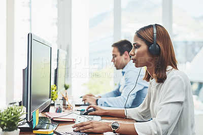 Buy stock photo Shot of two focussed young businesspeople working on their computers while speaking to clients over the phone in the office