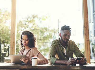Buy stock photo Shot of two young people using their wireless devices in a coffee shop