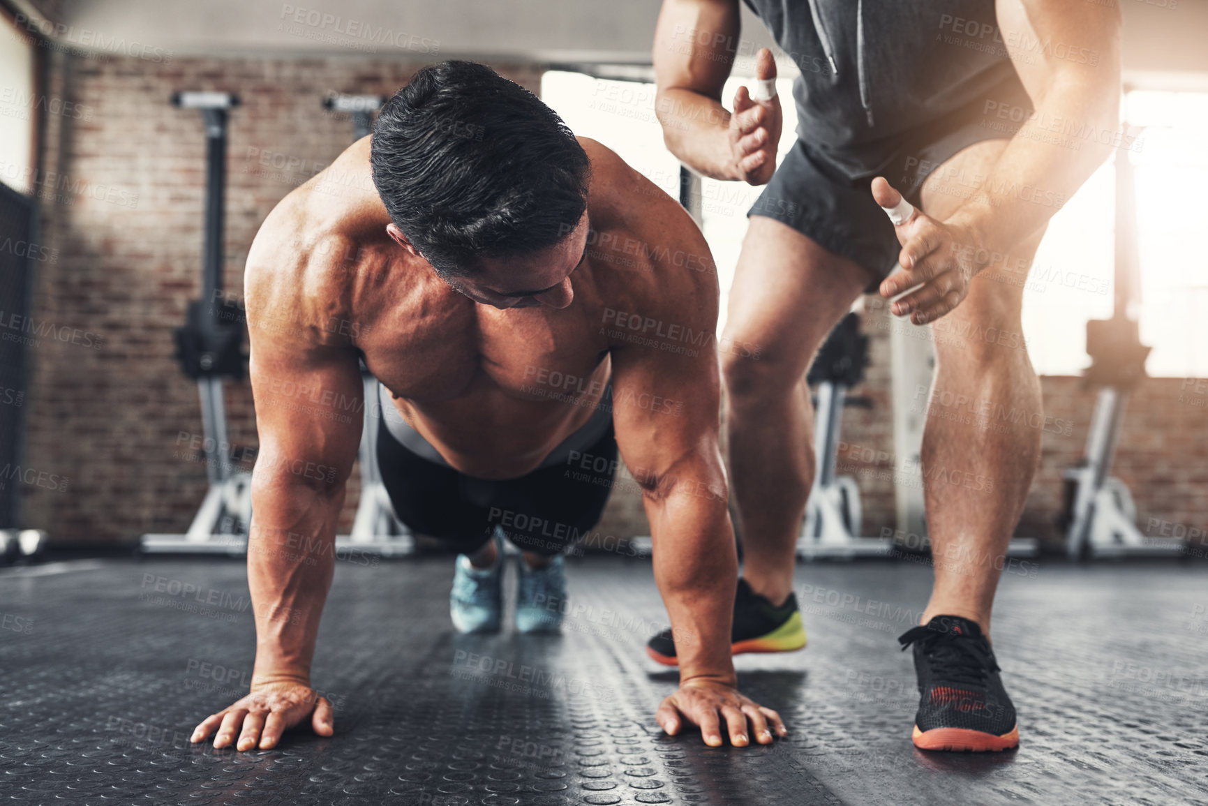 Buy stock photo Shot of a muscular young man working out with his fitness trainer in a gym