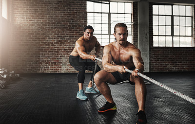 Buy stock photo Shot of two muscular young men pulling on a rope in a gym