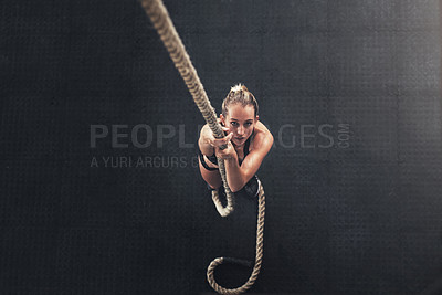 Buy stock photo Shot of a sporty young woman climbing a rope in a gym