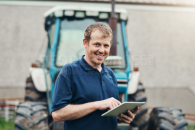 Buy stock photo Portrait of a cheerful young male farmer browsing on a digital tablet with his tractor in the background