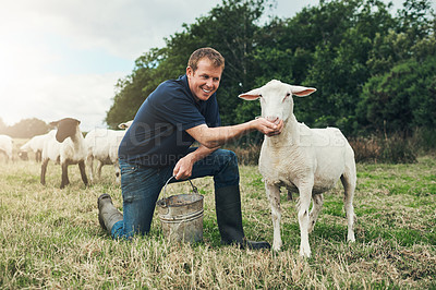 Buy stock photo Portrait of a cheerful young male farmer seated next to one of his sheep while feeding it outside on a farm during the day