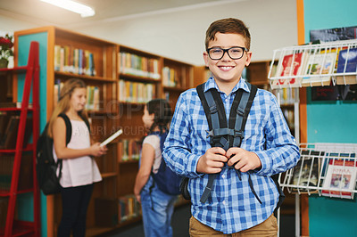 Buy stock photo Portrait of a cheerful young boy wearing a schoolbag while standing inside of library during the day