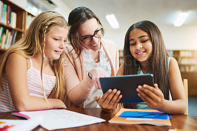 Buy stock photo Shot of two cheerful young school girls working together in a classroom with a digital tablet while being assisted by their teacher at school