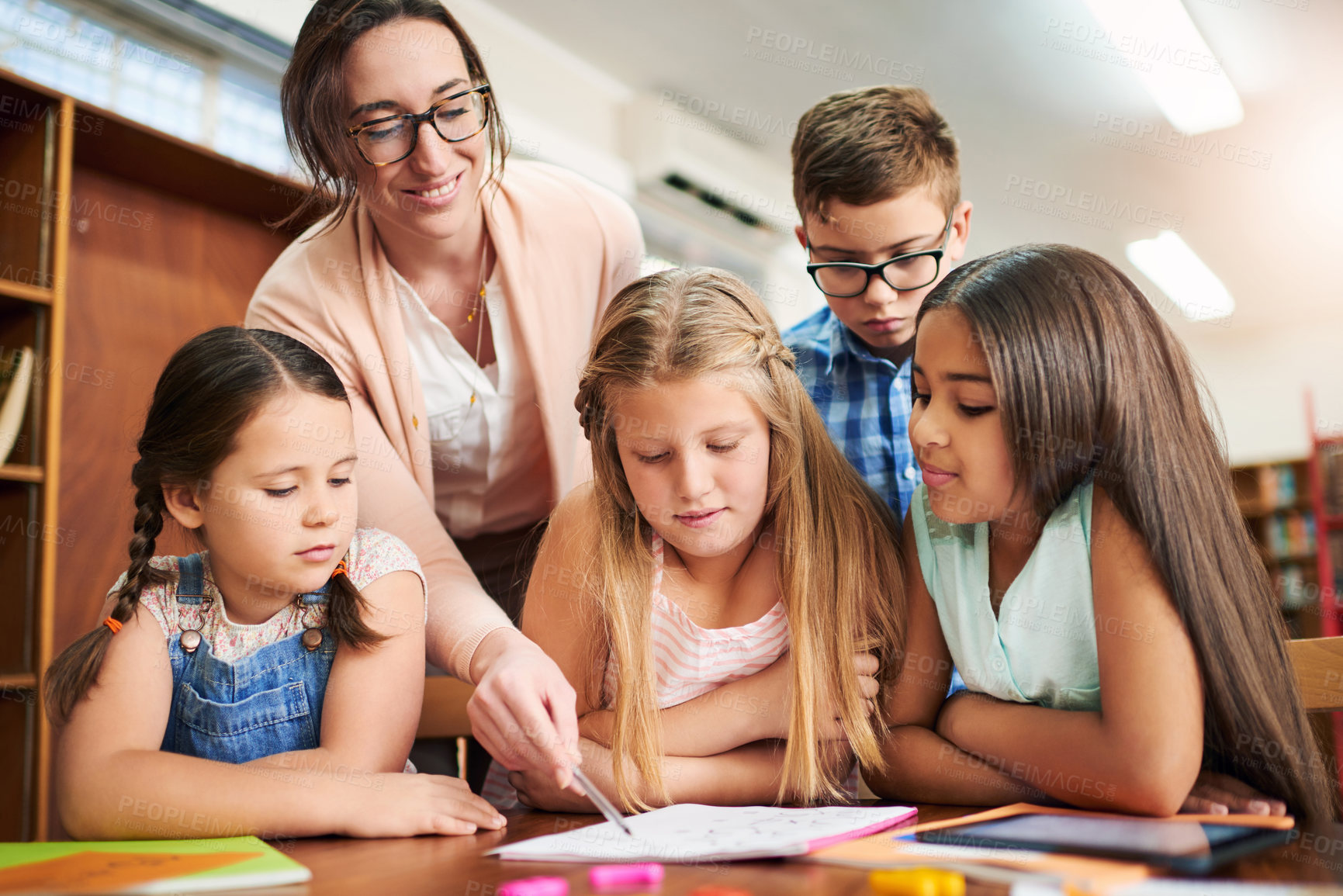 Buy stock photo Shot of a group of cheerful young school girls working together in a classroom with a digital tablet while being assisted by their teacher at school