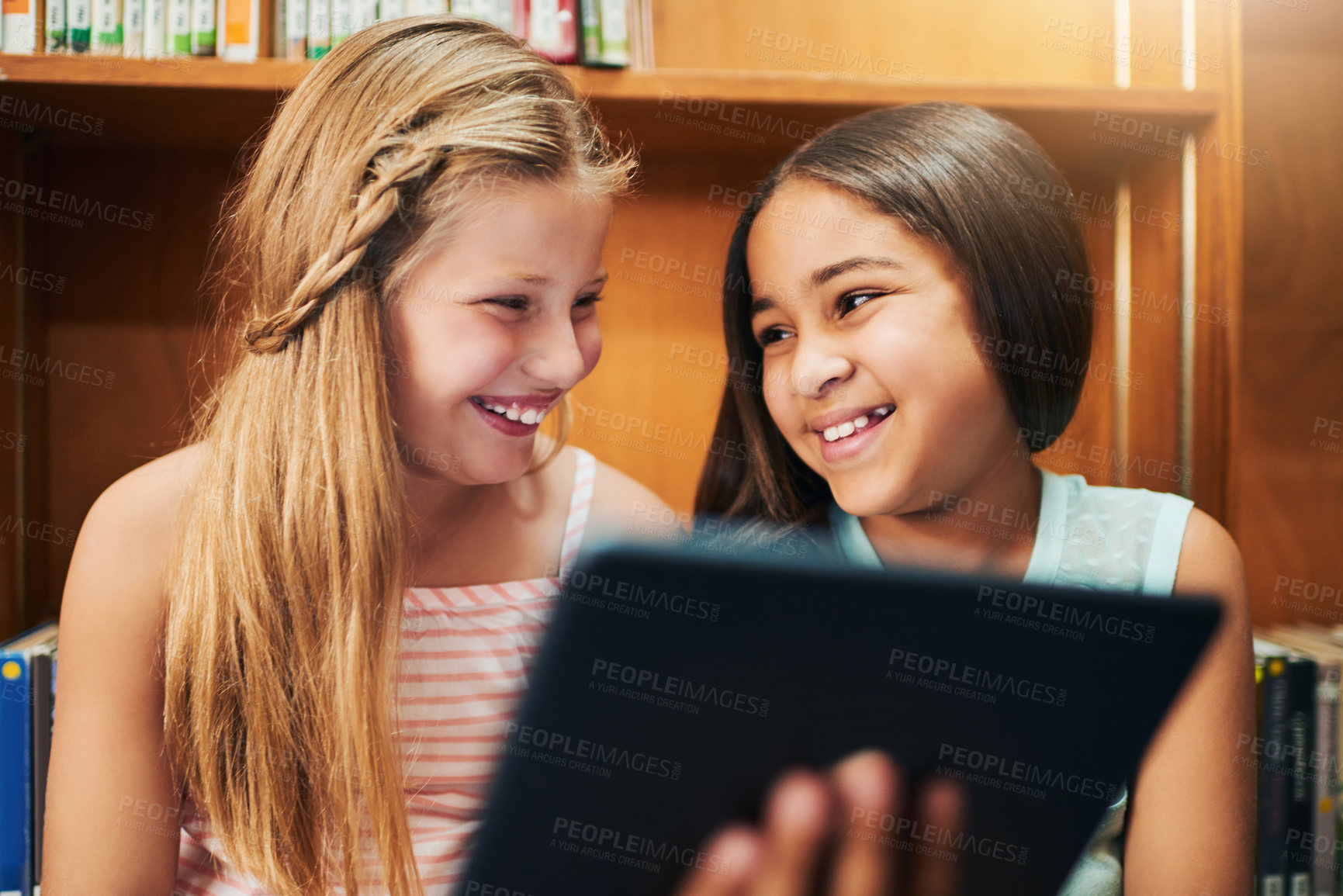 Buy stock photo School kids, girls or happy in library with tablet for educational games, reading ebook or watching videos. Friends, student or digital app at academy for online assessment, exam research or learning