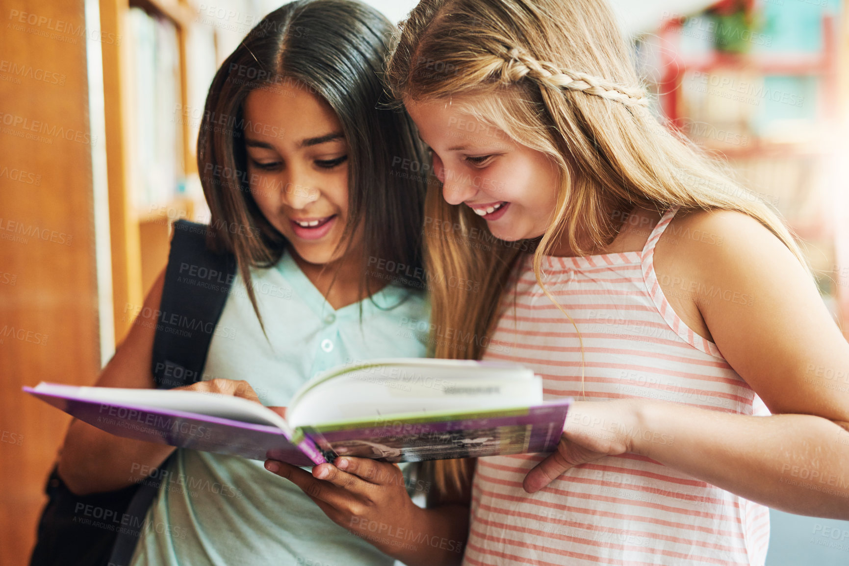 Buy stock photo Shot of two young school girls reading a book together while standing inside of a classroom during the day