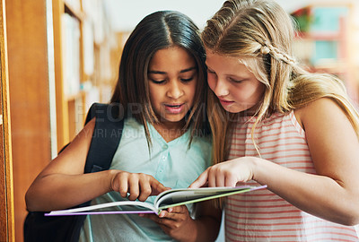 Buy stock photo Shot of two young school girls reading a book together while standing inside of a classroom during the day