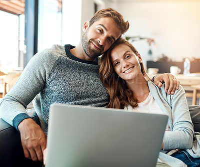 Buy stock photo Portrait of an affectionate young couple using a laptop while relaxing on their sofa at home