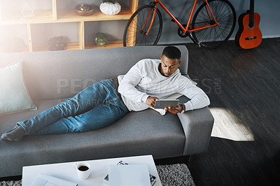 Buy stock photo Man, relax and tablet in home on sofa, networking and social media for online streaming in living room. Happy, research and technology on website, elearning and reading internet blog in apartment